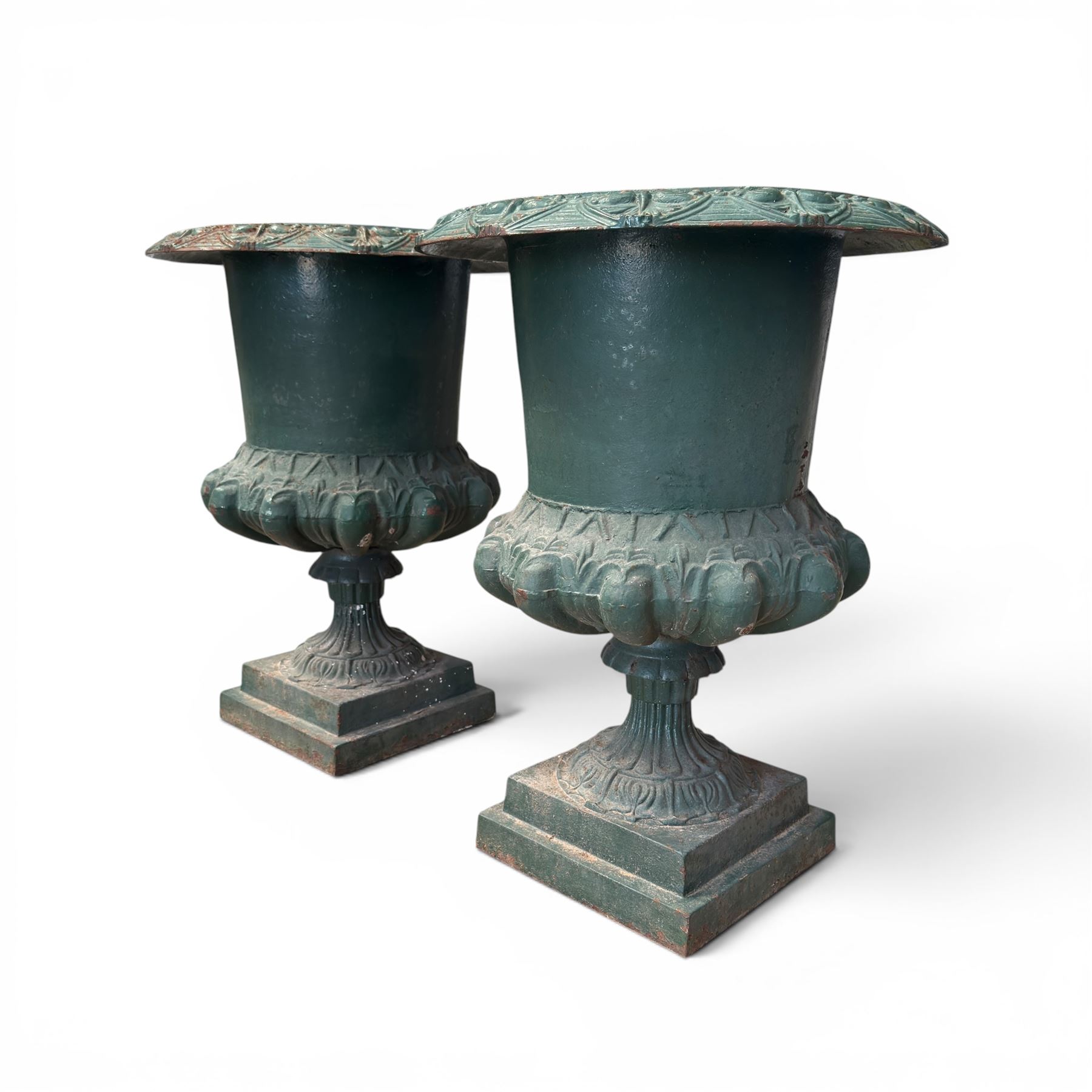 Pair of Victorian cast iron campana garden urns, the flared rim with repeating stylised anthemion motifs with scrollwork, over a deep gadrooned and Aesthetic moulded underbelly, fluted and foliate lower bowls on square pedestal bases, in antique green-painted finish