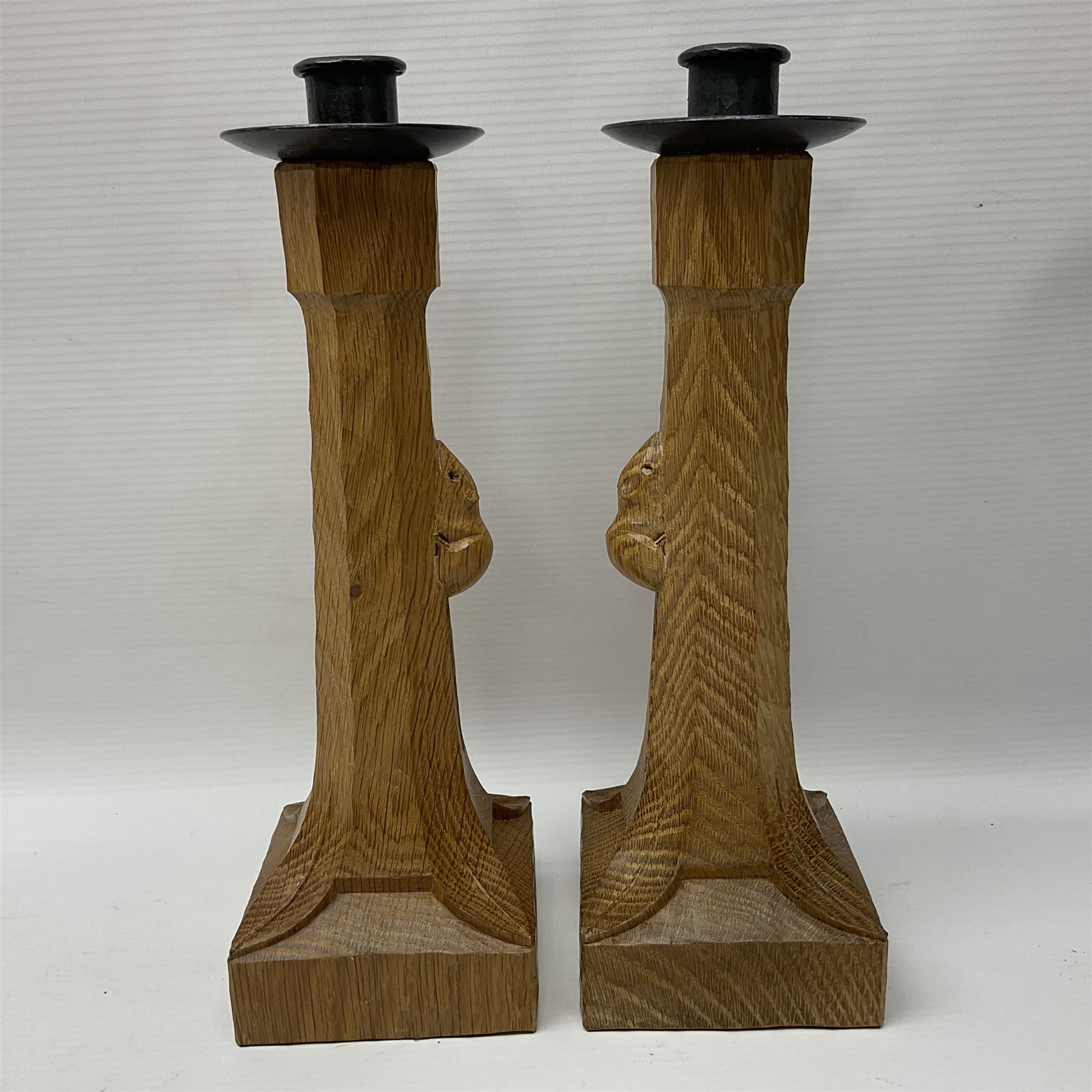 Mouseman - pair of tooled oak candlesticks, wrought iron sconce with drip tray over tapered octagonal column carved with mouse signature, terminating to stylised leaf carved square base, by the workshop of Robert Thompson, Kilburn
