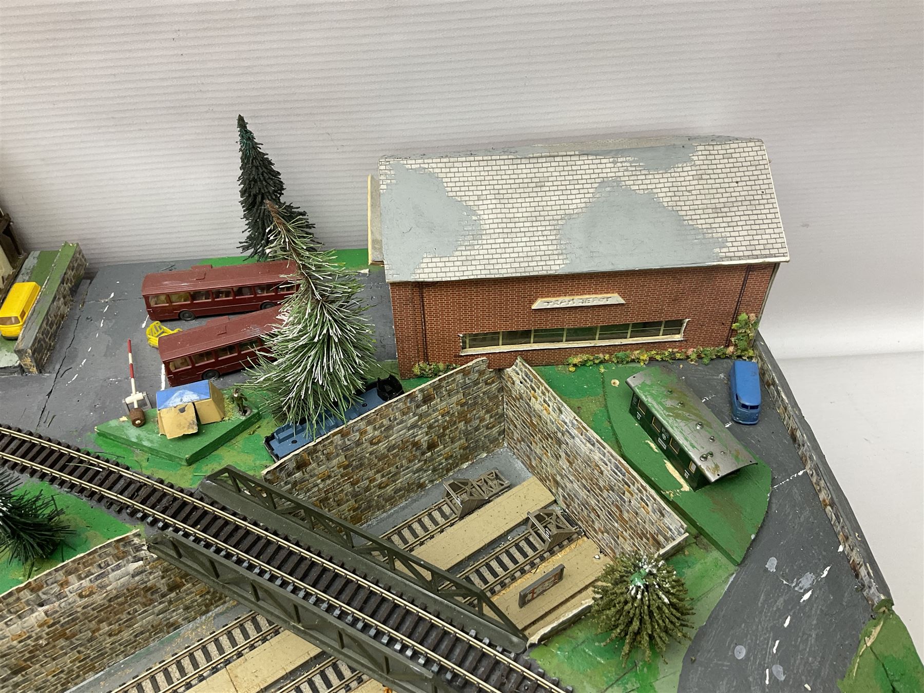 Table top 'N' gauge continental scenic layout as a split level town with various loops of track, station with numerous platforms, engine shed, assorted buildings, roads with motor vehicles and figures, tunnels, trees, river with bridge, tram depot etc 122 x 52cm