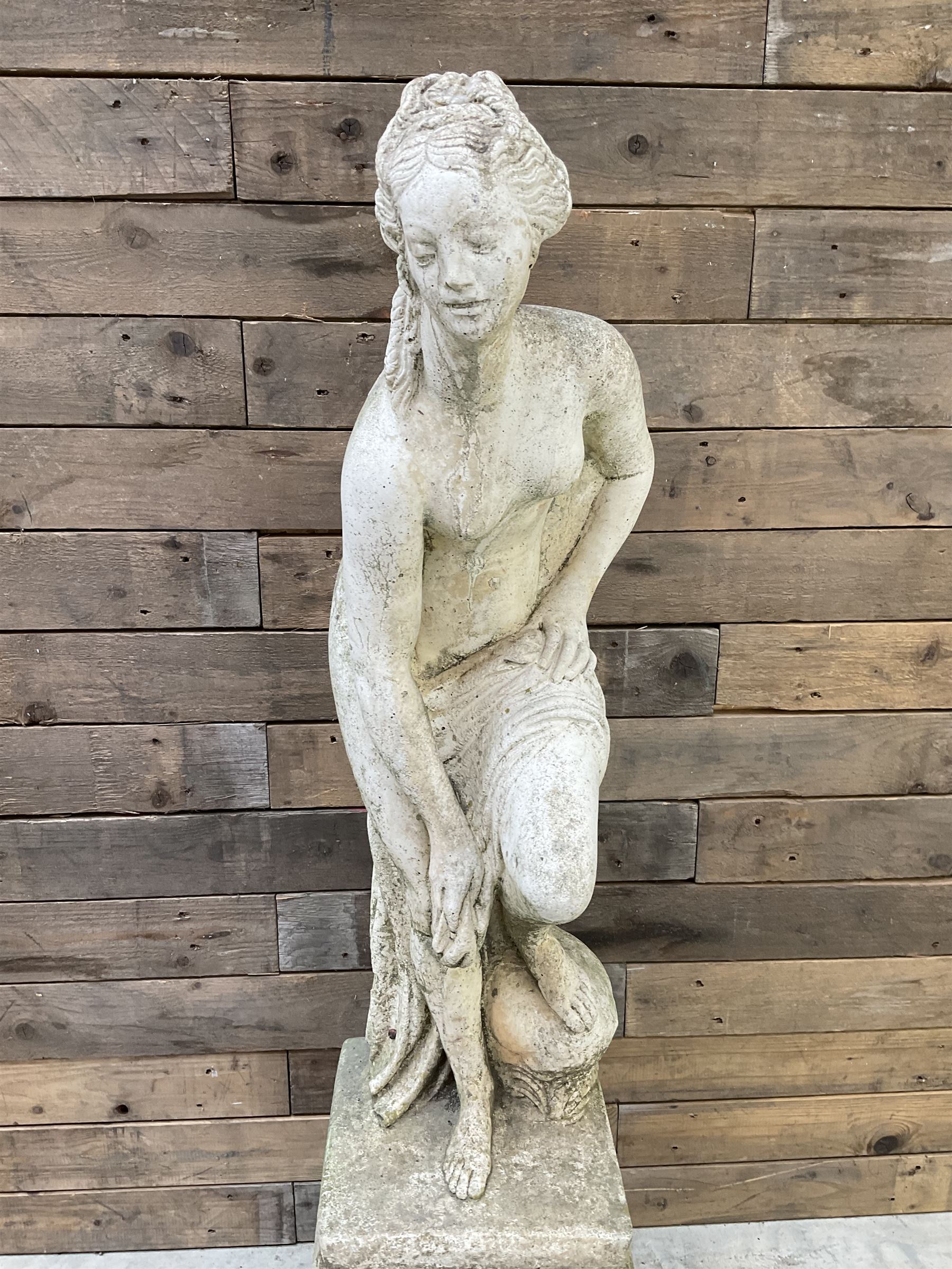 Cast stone garden statue of partially draped classical female figure on ornate pedestal 