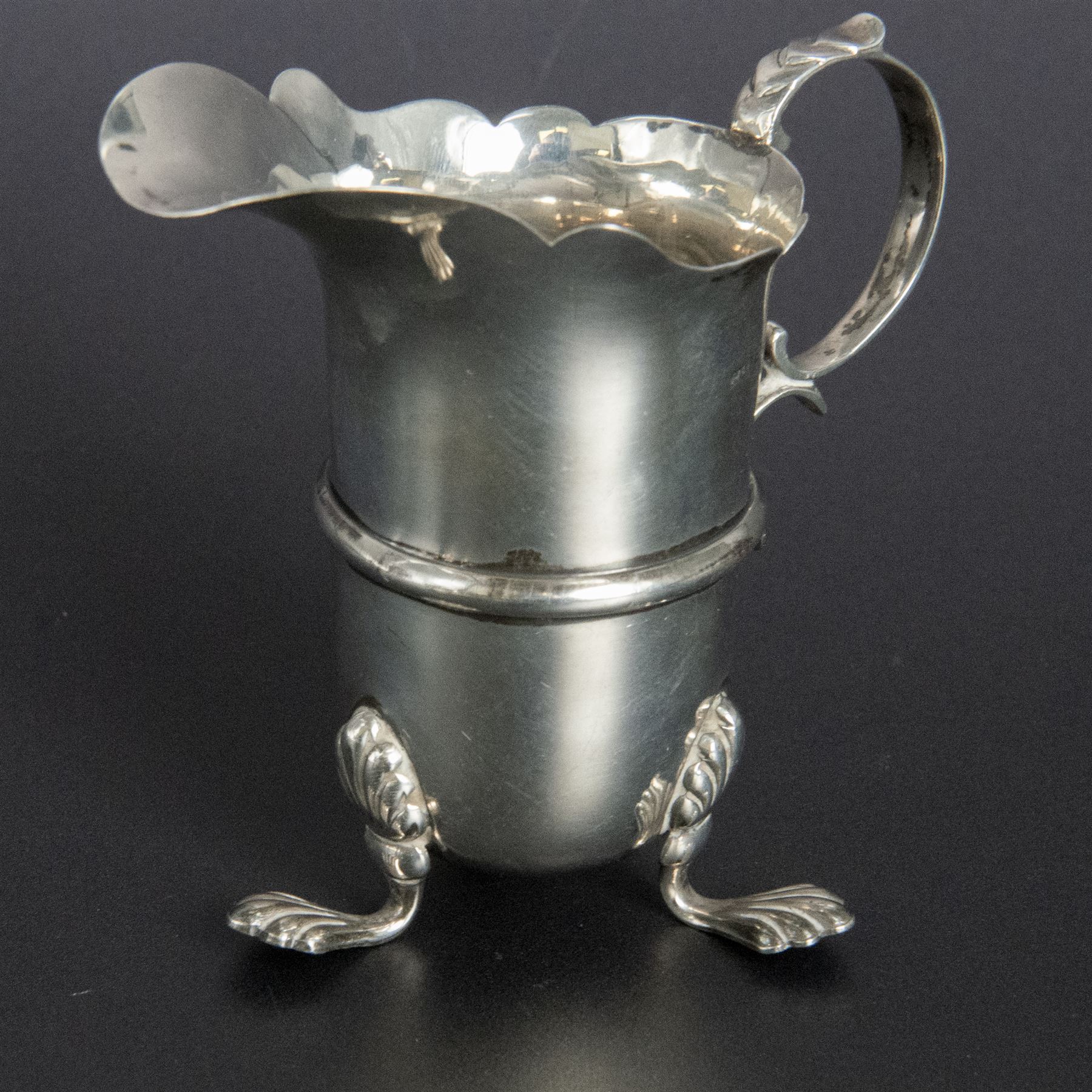 Group of early 20th century silver, comprising sauce boat, with flying scroll handle and upon three pad feet, two small cream jugs and a christening mug, all hallmarked, tallest H10cm