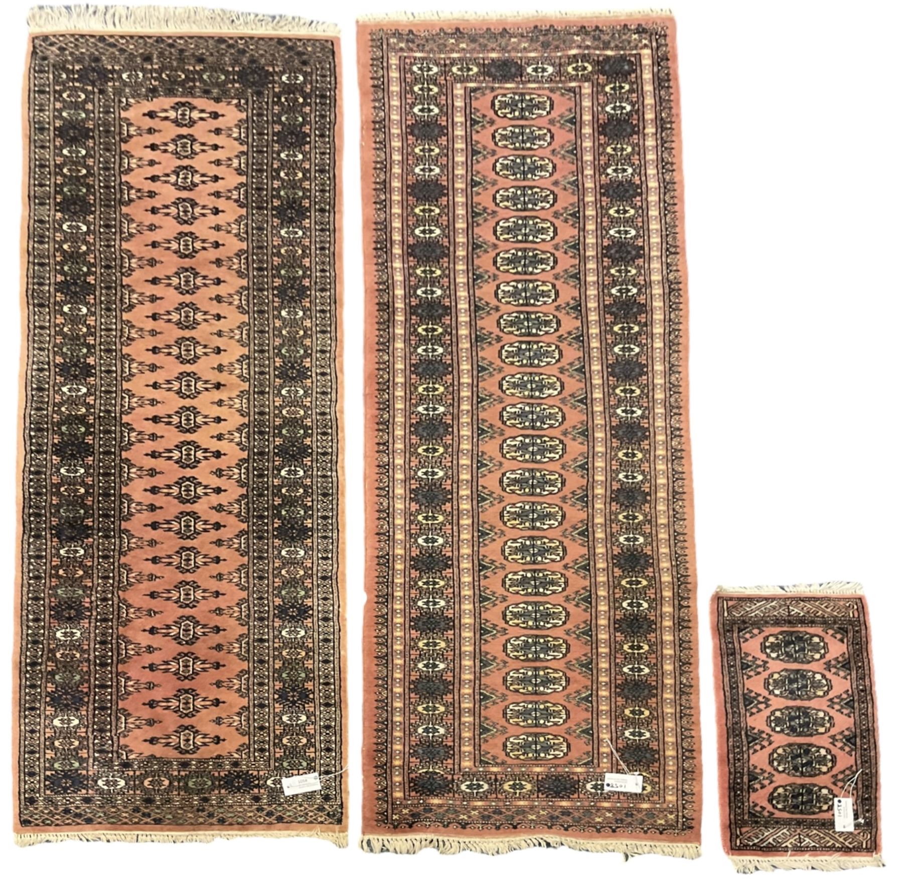 Bokhara peach ground runner, decorated with a single row of Gul motifs (192cm x 67cm); a similar peach ground runner (185cm x 67cm); and a small Bokhara mat (58cm x 32cm)