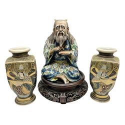 Late 20th century Japanese figure of a sage, partially glazed, modelled sitting cross-legged pointing to a tablet laid in his palm, his head with long hair and horns and his blue robe with leaves in greens, blues and grey, with pierced circular display stand, together with pair of Japanese satsuma vases, tallest H16cm