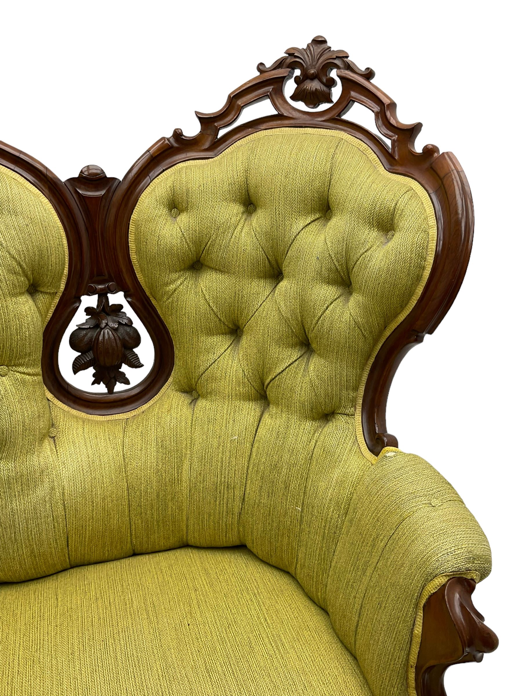 Victorian walnut settee, triple back with pierced and scroll-carved cresting rails over carved fruit and foliage decoration, upholstered in buttoned green fabric, serpentine seat and carved apron, on cabriole feet