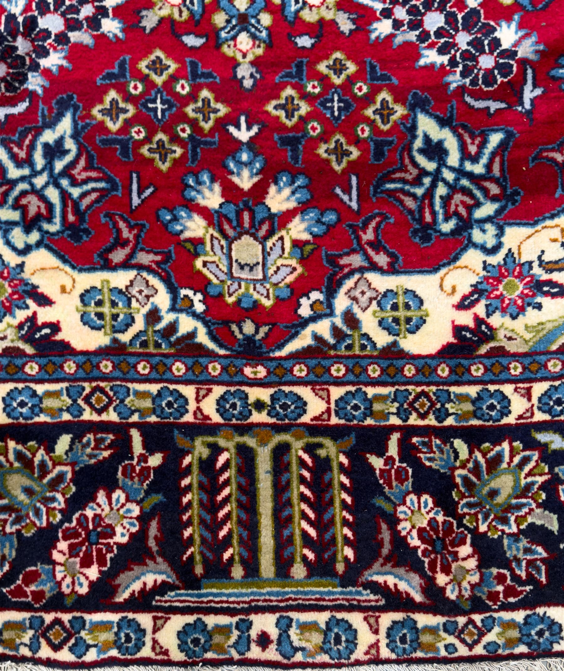 Central Persian Isfahan Carpet, hand-knotted, featuring a bold central rosette medallion on a rich red field, flanked by stylised floral sprays, scrolling foliage and mythical animals, within a broad indigo border decorated with alternating cartouches and flowerheads