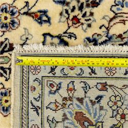 Central Persian Kashan hand-knotted rug, ivory ground, with a small central floral medallion and pendants, the field finely decorated with blue, cream and soft red scrolling vines, flowerheads and palmettes, within an ivory floral border and narrow guard stripes, with cotton fringes