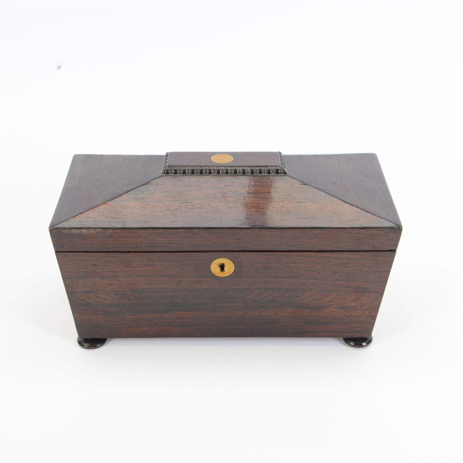19th century rosewood sarcophagus shaped tea caddy, the hinged lid with brass cartouche to the centre, opening to reveal a fitted interior with central glass bowl flanked and lidded compartments to either side, upon squat bun feet, H17cm