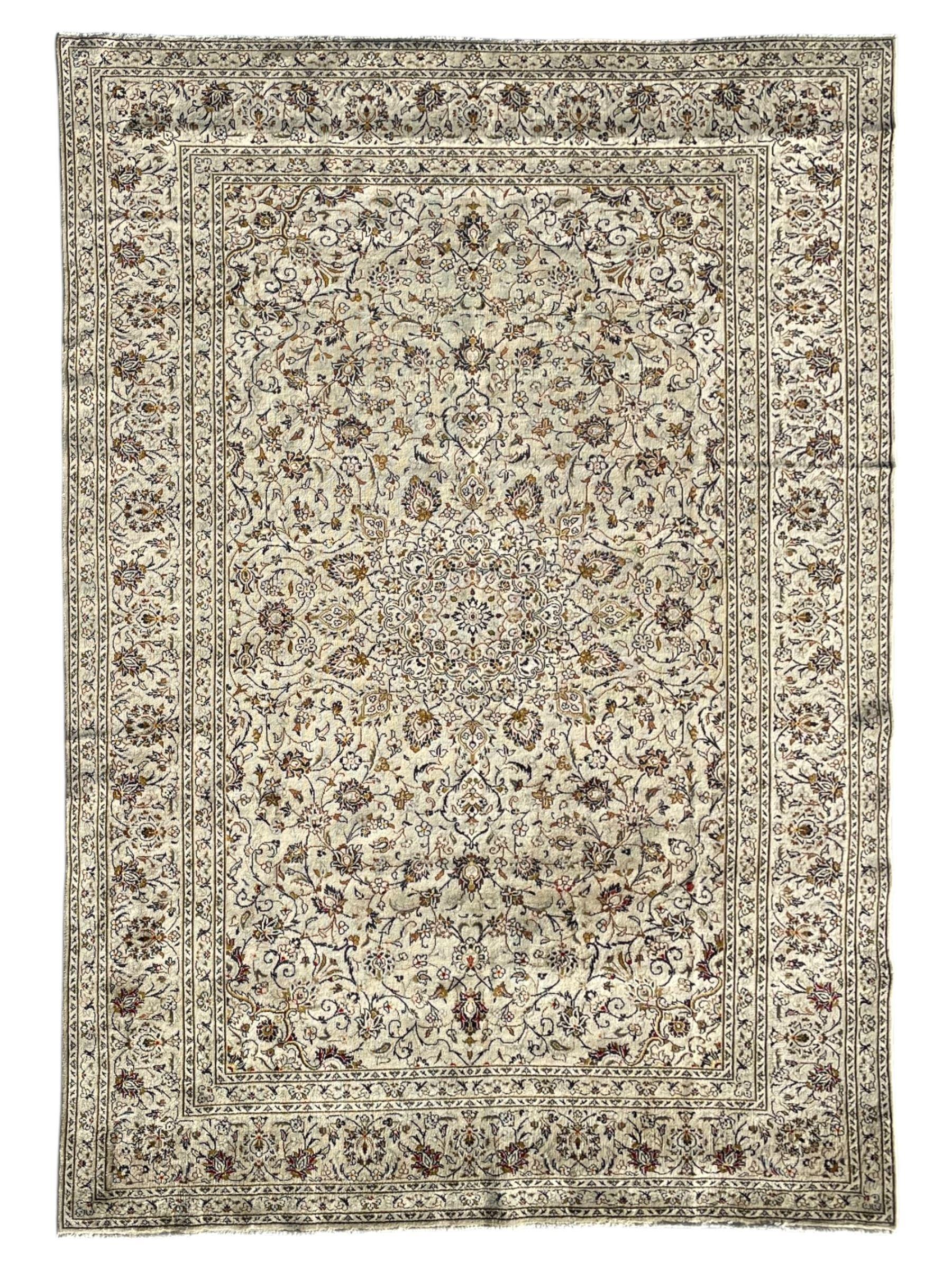 Persian Kashan ivory ground carpet, central medallion decorated with sixteen arranged palmette motifs, within a field decorated with swirling leafy branches and stylised plant motifs, the main border decorated with matching swirling pattern, within floral pattern guard stripes 