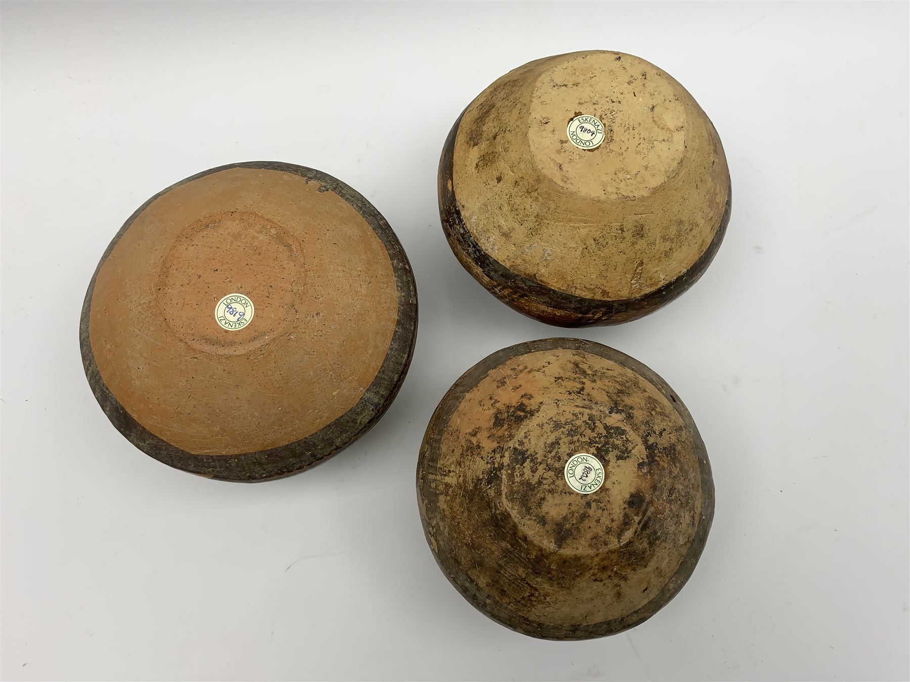 Three Chinese Neolithic pottery vessels, each with twin loop handles to the shoulder and painted geometric banded decoration to the body, all bearing labels for Eskenazi London, tallest H14cm