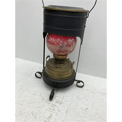 Brass oil lamp with red painted glass shade encased in black metal with handle and four feet, H54cm excl handle 
