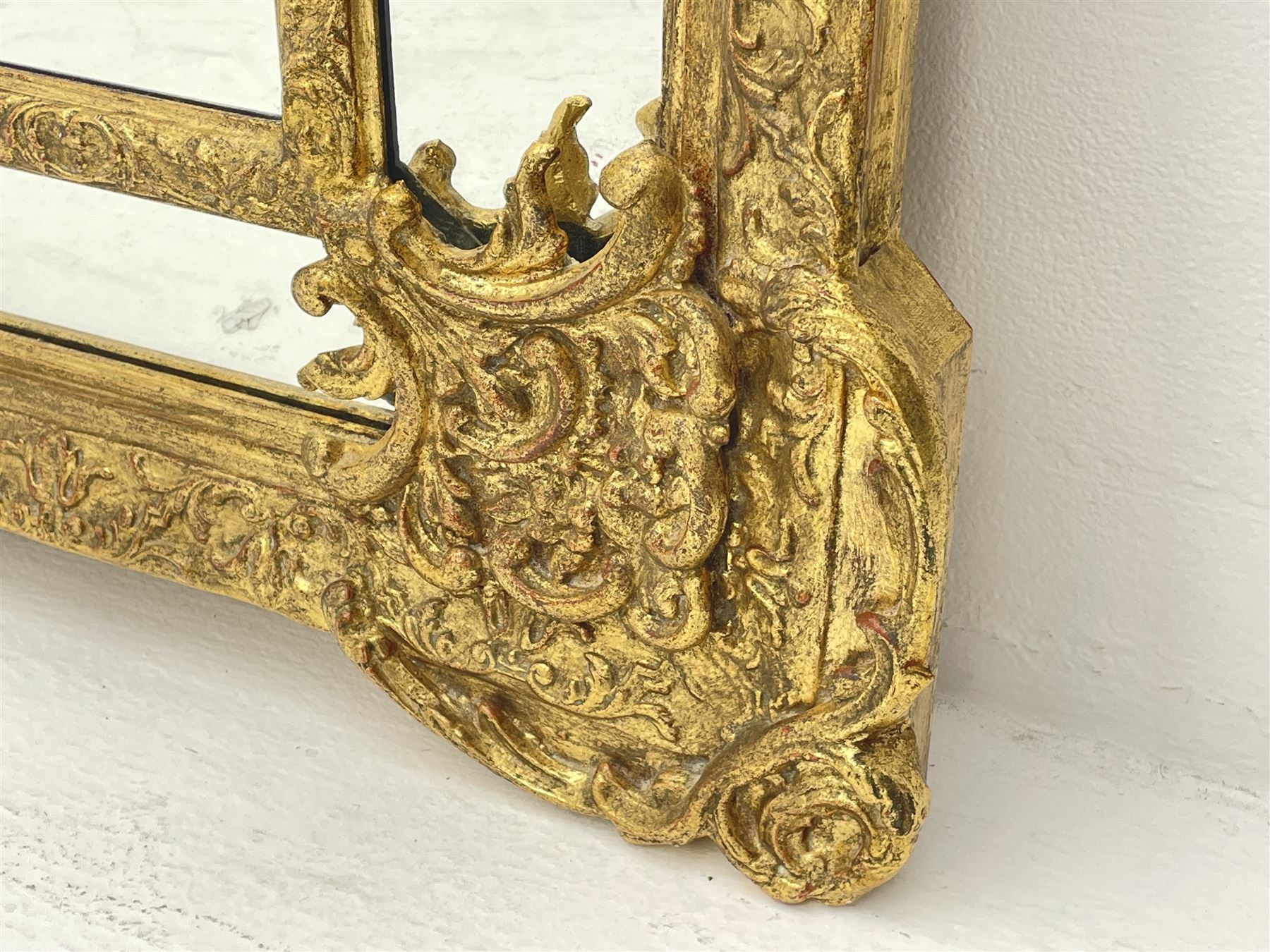 Large Victorian style gilt cushion framed mirror, putti holding urn with scrolled foliage pediment above central rectangular bevelled plate, the frame decorated with moulded foliate, each corner set with ornate cartouche