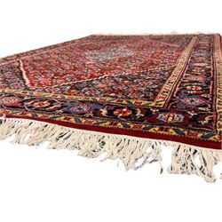 Persian crimson ground rug, central light blue lozenge medallion with floral motifs, the densely decorated crimson field filled with repeating flower heads and trailing leafy vines, the black and red border with interlacing foliate patterns and floral cartouches, surrounded by guard stripes