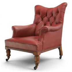 Early 20th century style oxblood red leather Chesterfield armchair, deep buttoned shaped back over padded scroll arms and loose seat cushion, raised on turned mahogany front supports with brass caps and castors