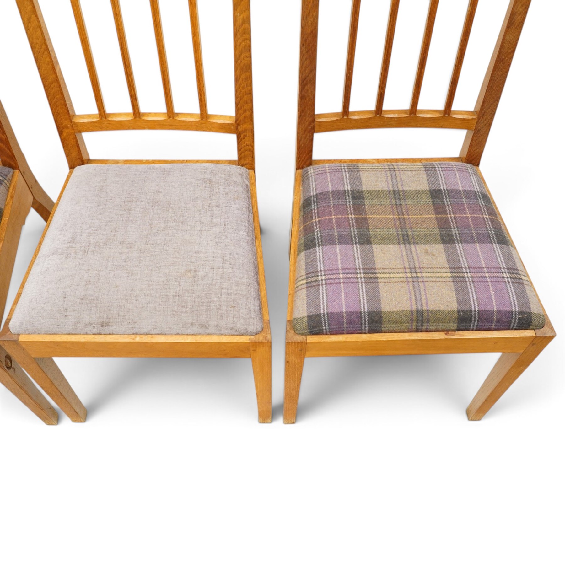 Acorn Industries - set of eight oak dining chairs, the shaped cresting rail over a fluted stick back, the drop-in seats upholstered in contrasting form with four pale mauve and four in purple tartan, raised on square supports, carved with acorn signature, by Alan Grainger, Brandsby
