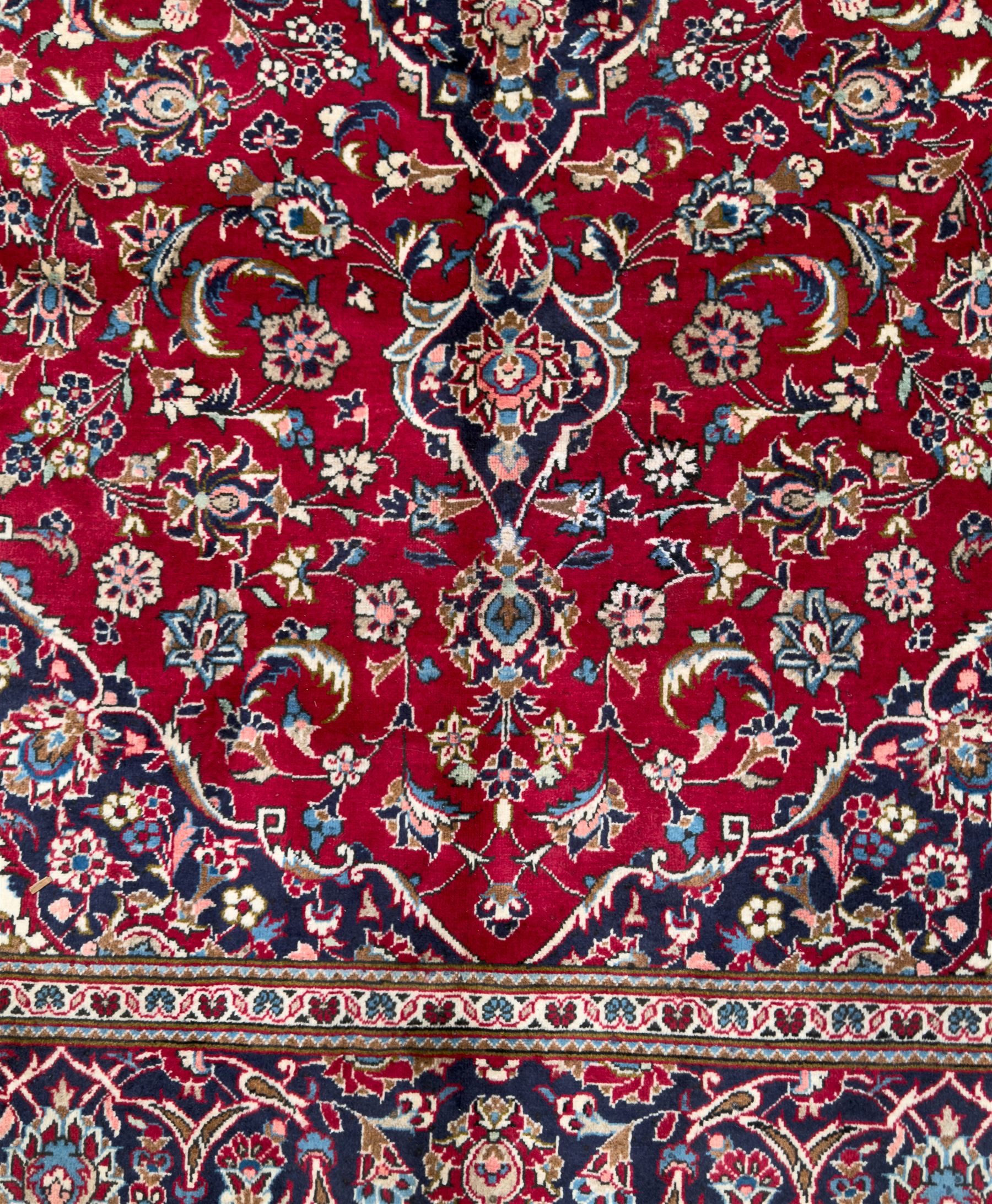 Central Persian Kashan hand-knotted carpet, the deep red ground with a central lozenge medallion in ivory and navy, surrounded by dense scrolling floral and vine motifs, navy spandrels and a wide border with stylised palmettes and flowerheads enclosed by multiple guard stripes