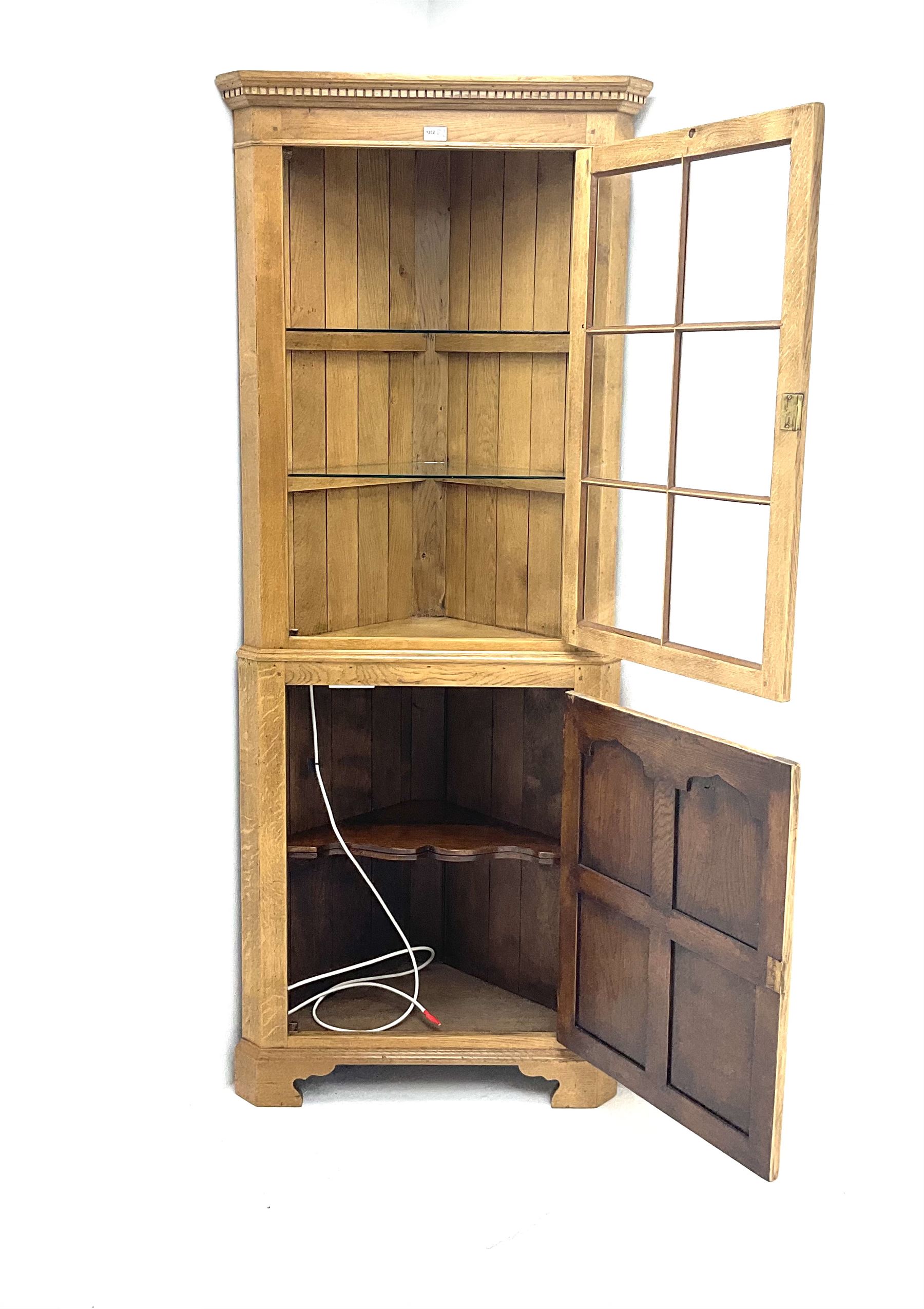 Oak corner cabinet, projecting cornice, dentil frieze, single glazed door enclosing two glass shelves above bottom unit, single fielded door enclosing fitted interior 