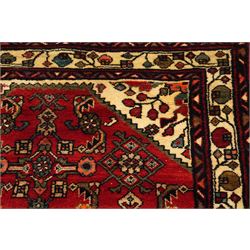 Large Persian Qashqai runner rug, the red ground decorated with navy and ivory lozenge medallions interspersed with stylised floral and geometric motifs, enclosed by an ivory flowerhead border and patterned guard stripes