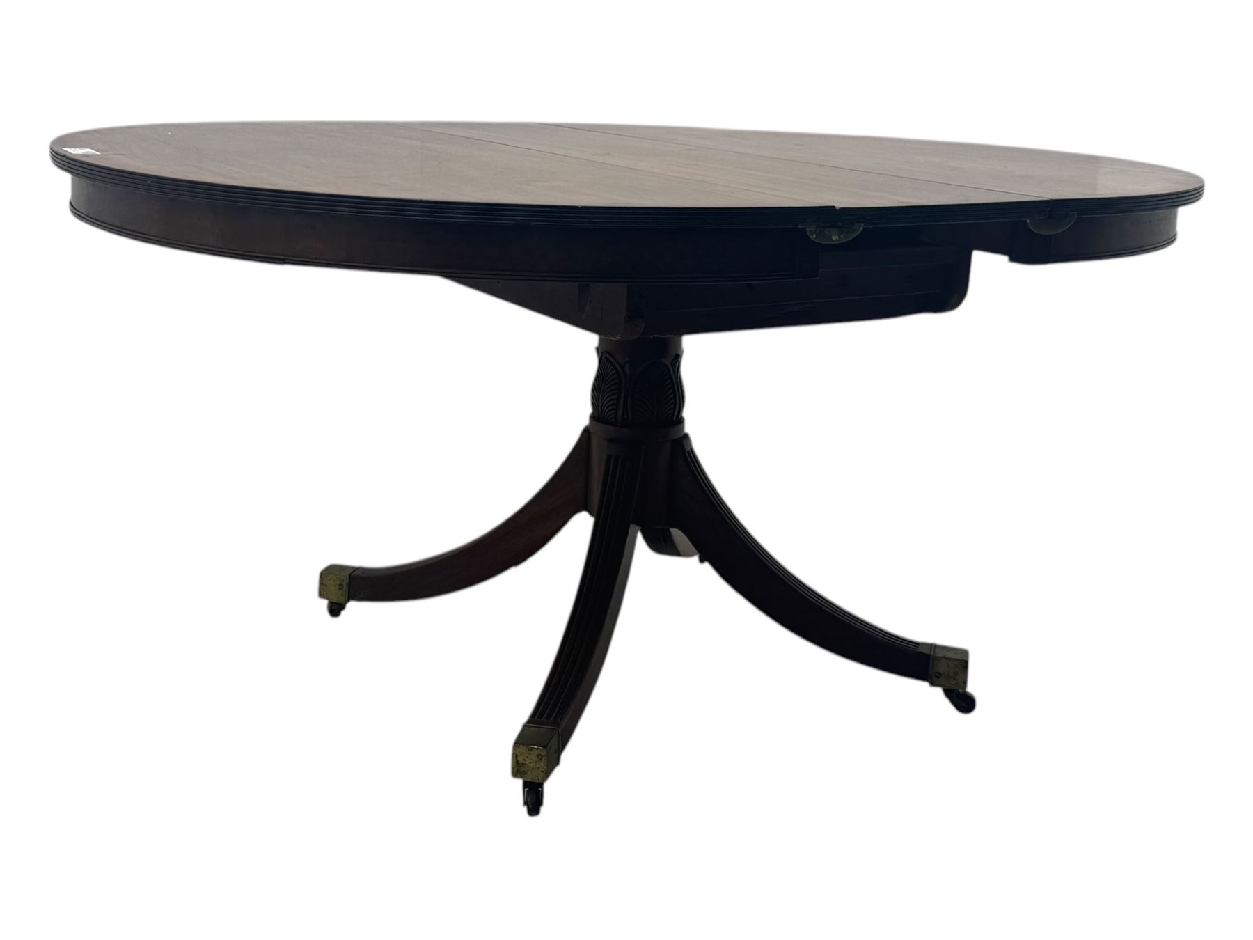 Regency design mahogany extending dining table, circular top with reeded edge and pull-out mechanism to accommodate additional leaf, raised on a carved central baluster column with acanthus detailing, supported by a quadruple reeded splay base terminating in brass caps and castors

