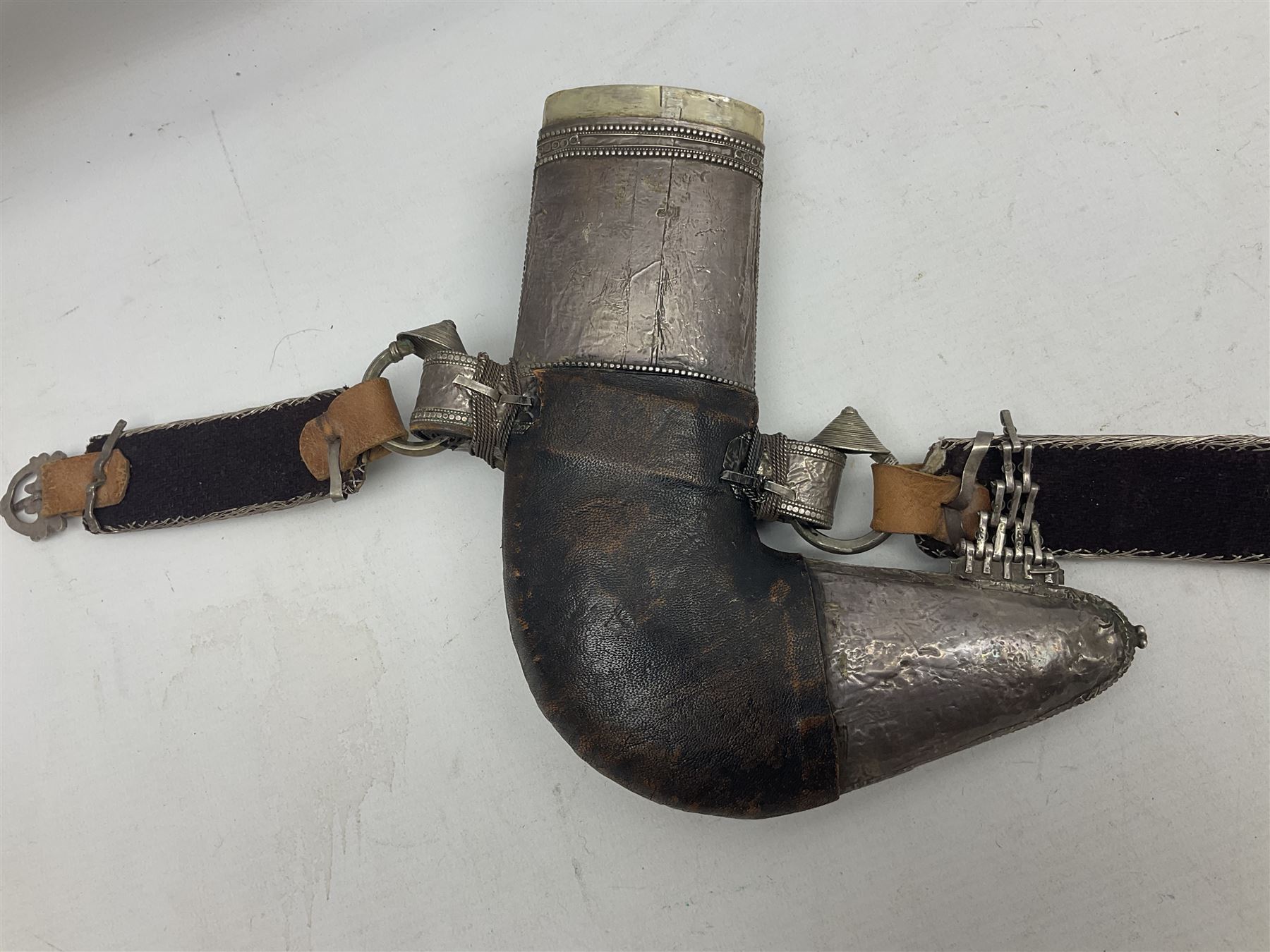 Omani Khanjar dagger, the 19cm curved blade with pronounced medial rib to either side, waisted hilt with dome shaped pommel and silver covered horn grip decorated with filigree bands, floral motifs and beadwork; in an intricately filigree decorated silver and leather scabbard with silver rings woven into the belt mount and fitted with original silver thread-work belt L34cm overall belt length 94cm