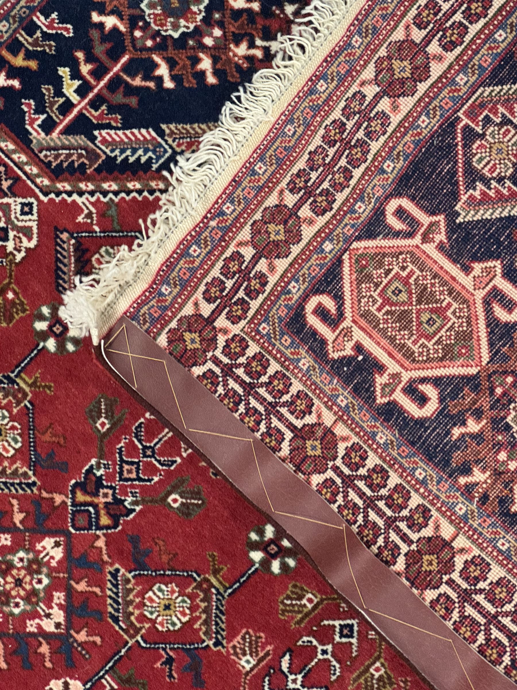 Persian Qashqai crimson ground runner, the central field decorated with three large geometric medallions with intricate angular and floral motifs, the indigo spandrels with complementary geometric designs, bordered by an ivory band with repeating floral patterns and angular vines