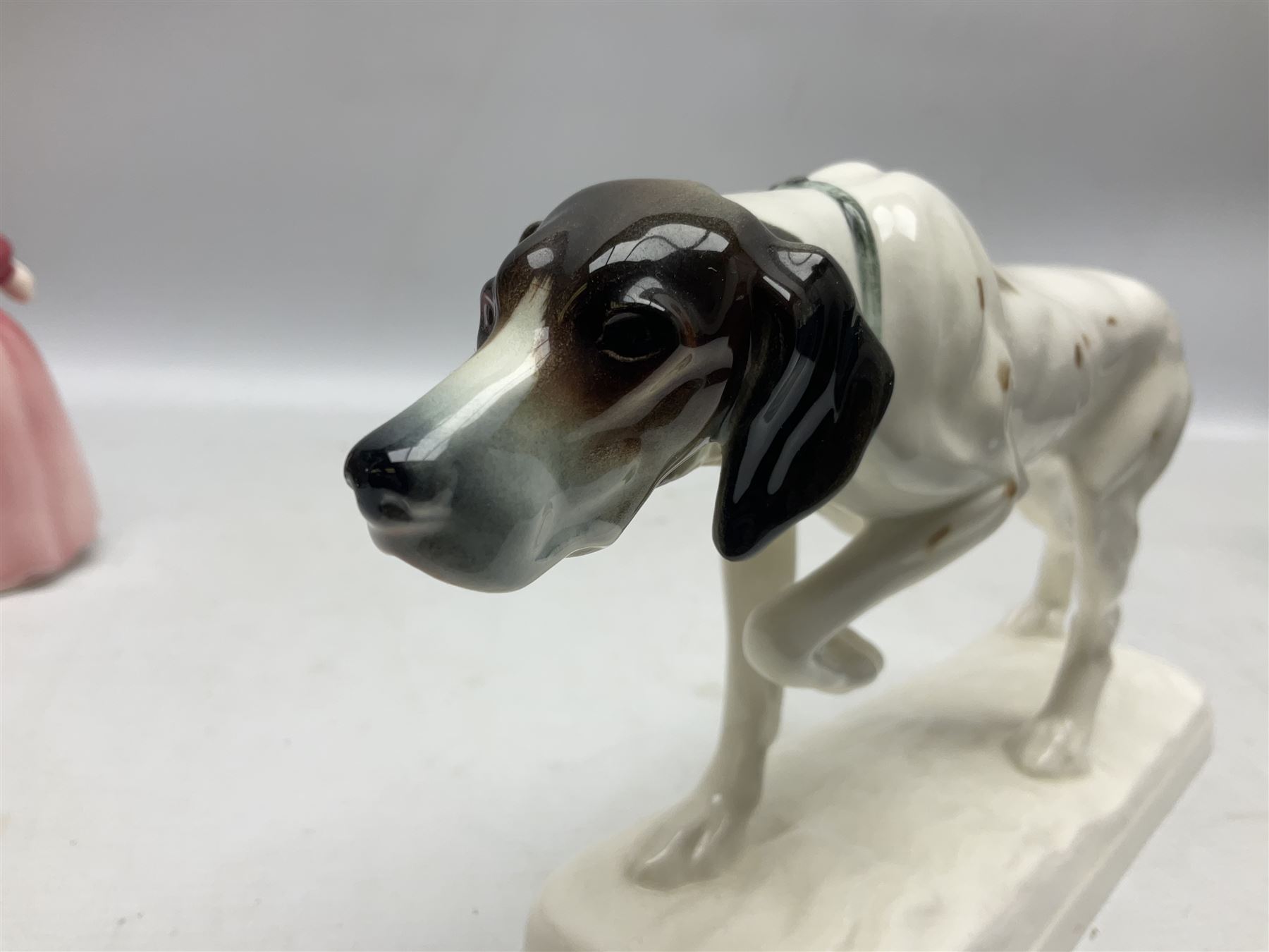 Early 20th century Katzhütte figure of a pointer dog, and figure of a young girl holding basket and fan, both with green cat H house printed mark beneath, dog L25cm