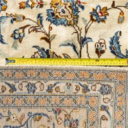 Central Persian Kashan rug, cream ground densely patterned with interlaced floral stems and rosettes in blue, gold and brown, framed by layered borders featuring stylised palmettes, woven in the Kashan weaving district of Iran