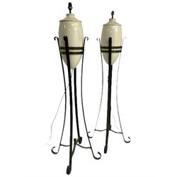 Pair of wrought metal and ceramic floor lamps, urn-shaped lamps in crazed cream glaze on wrought metal stands with four splayed supports 