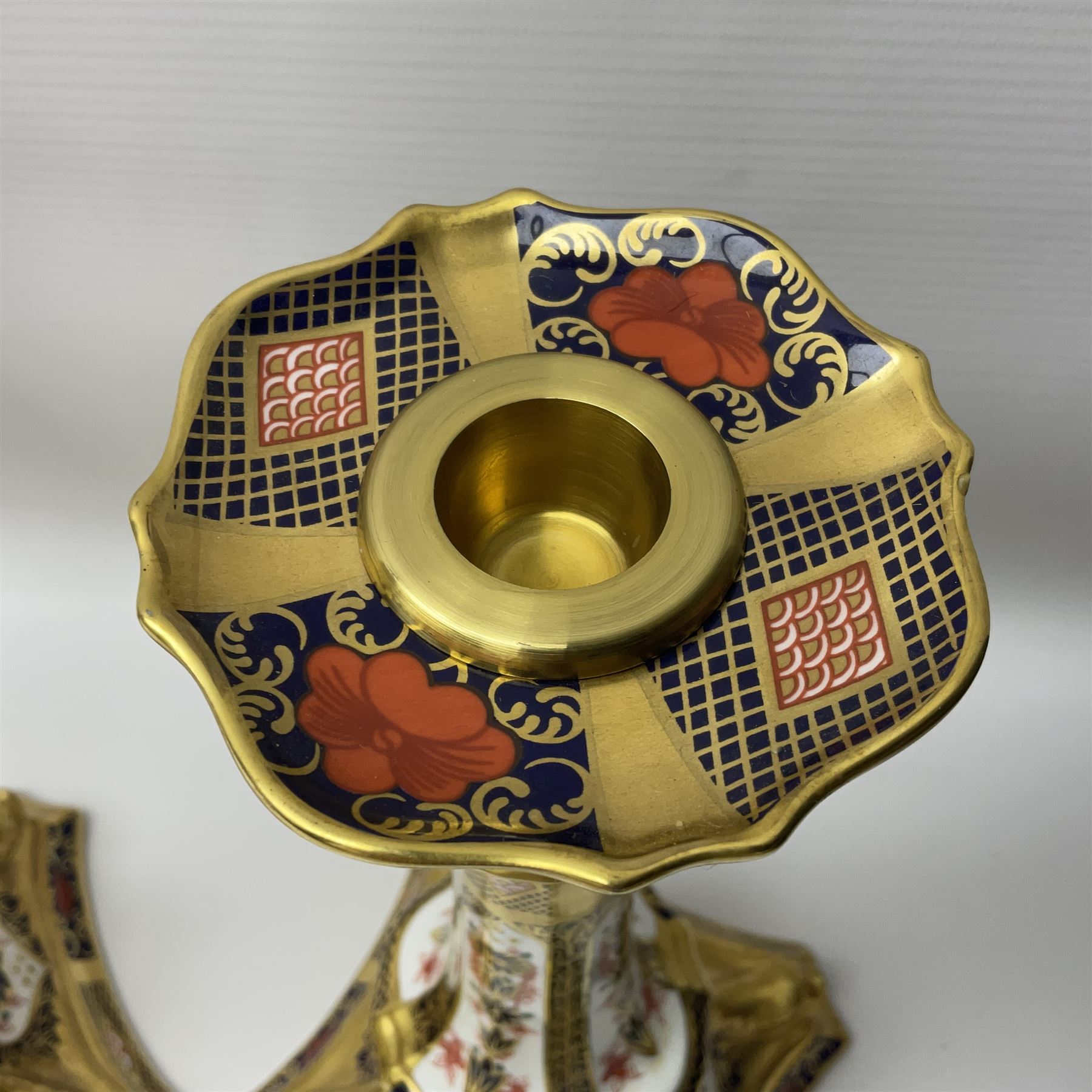 Pair of modern Royal Crown Derby Old Imari 1128 pattern candlesticks, each with shaped drip tray affixed to squat socket, upon spreading stem and canted square base with gilt dolphin edges, with printed marks beneath including Roman numeral year cypher for 2003, H26.5cm, with original boxes
