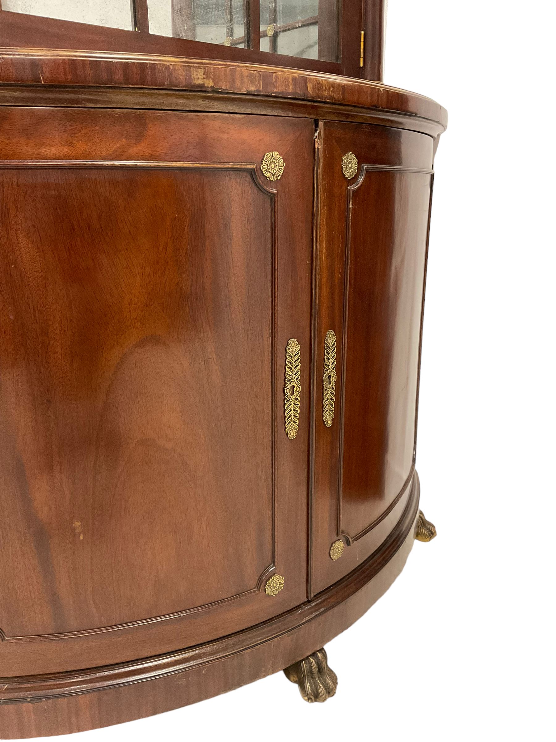 Pair of French Empire design corner cabinets, the straight-front upper section with canted corners and applied half-column pilasters, enclosed by mirror glazed door, the bow-front lower section enclosed by two doors with applied mouldings, mounted by cast metal floral rosettes, skirted base with cast gilt metal hairy paw brass feet