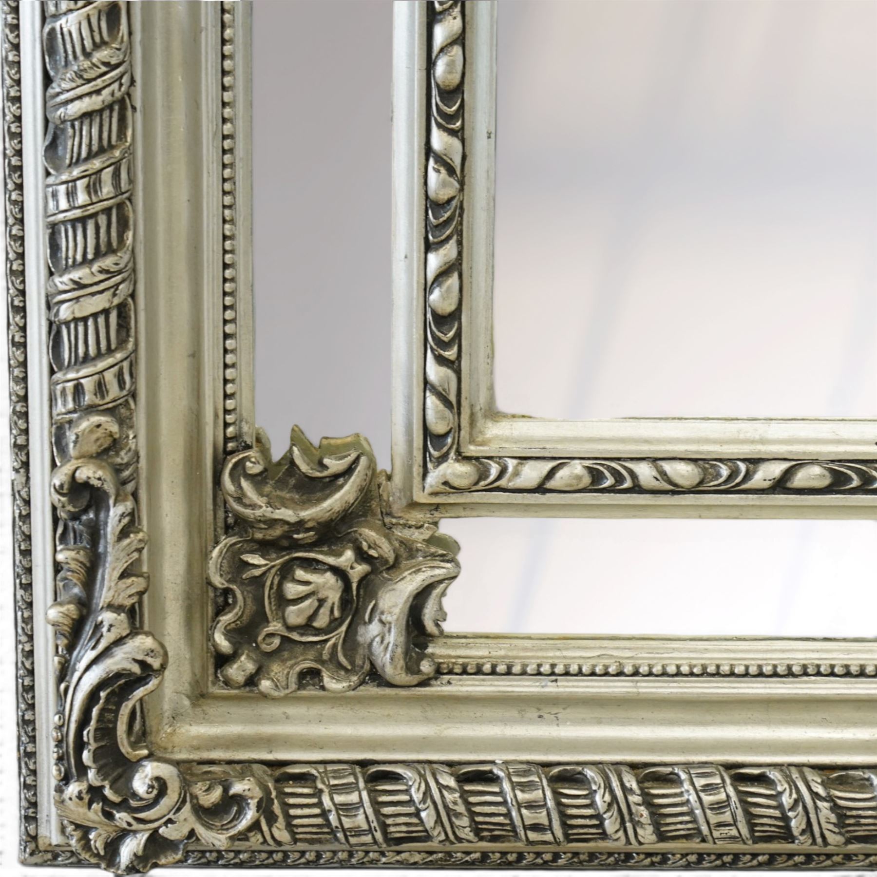 Impressive Baroque Revival mirror in antique silvered finish, the pierced cartouche shell pediment flanked  by C-scrolls and flower heads, the outer frame with ribbon-twist motifs throughout, the central arched bevelled plate surrounded by further rectangular mirror panels with cartouche mounts