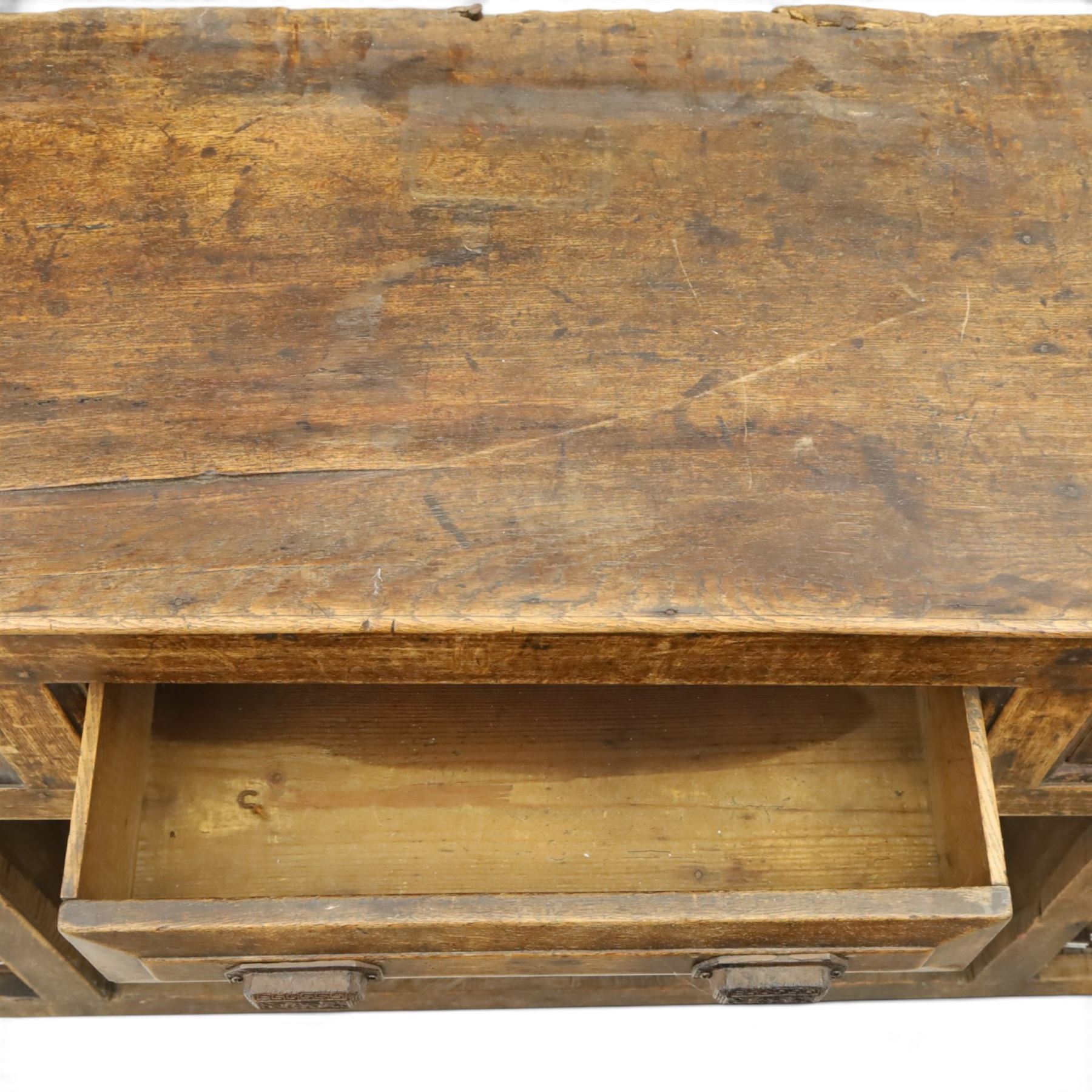 18th century rustic oak dresser base, with fielded panels and iron cup handles with embossed greek key and foliate detail, three short drawers above and open recess flanked by two cupboard doors, raised on stile supports