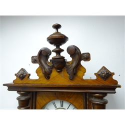  Late 19th century Vienna style walnut wall clock with carved pediment over a glazed door flanked by turned half columns enclosing an enamel dial with Roman numerals and subsidiary seconds dial, single weight driven movement and moulded base with finials H126cm  