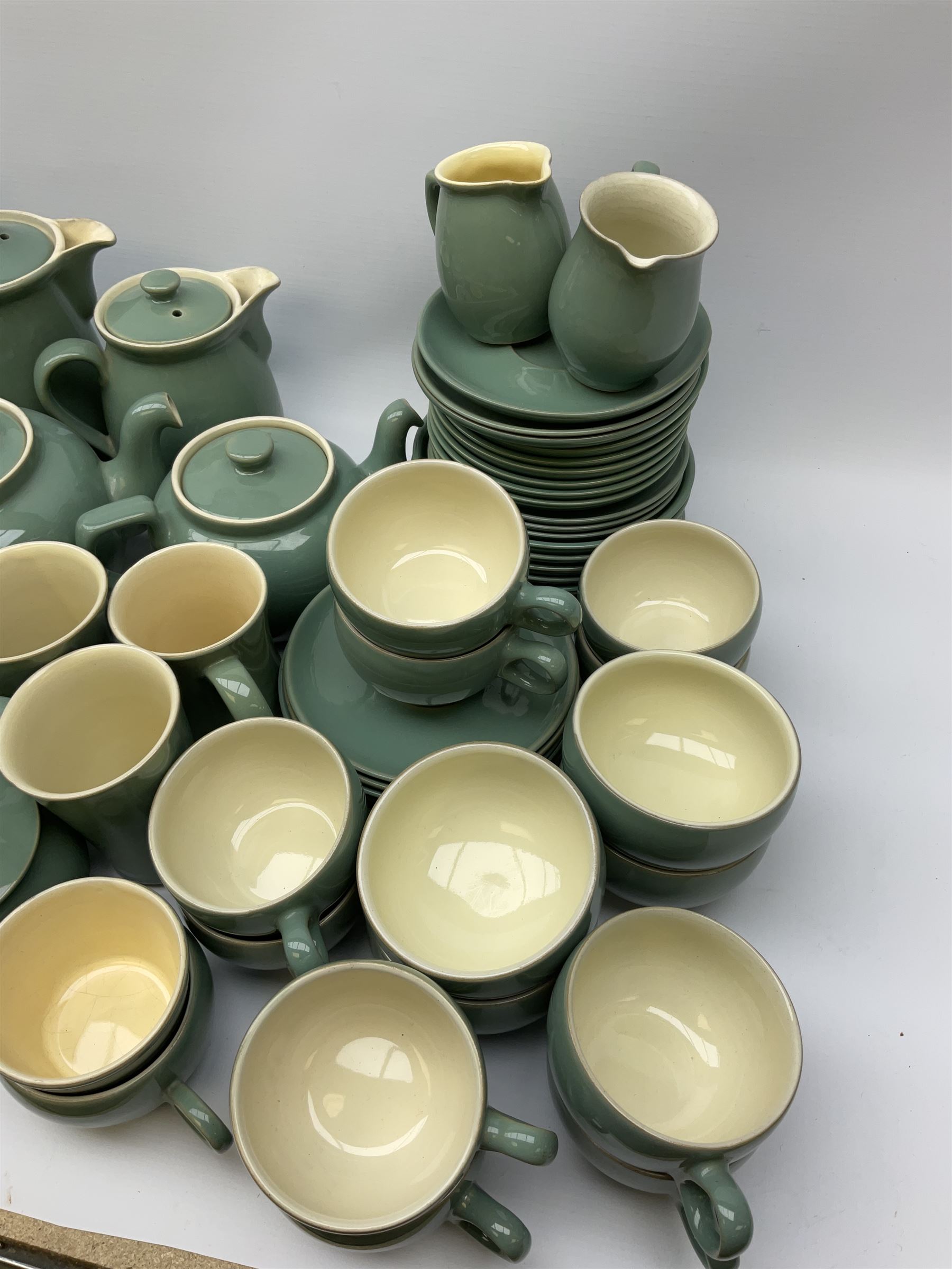 Denby Manor Green pattern tea service, comprising of three teapots, twelve coffee pots of various sizes, four hot water jugs with lids, seven jugs, eleven teacups, four mugs, seventeen saucers, six sugar bowls, two sugar bowls with lids and eleven side plates.  