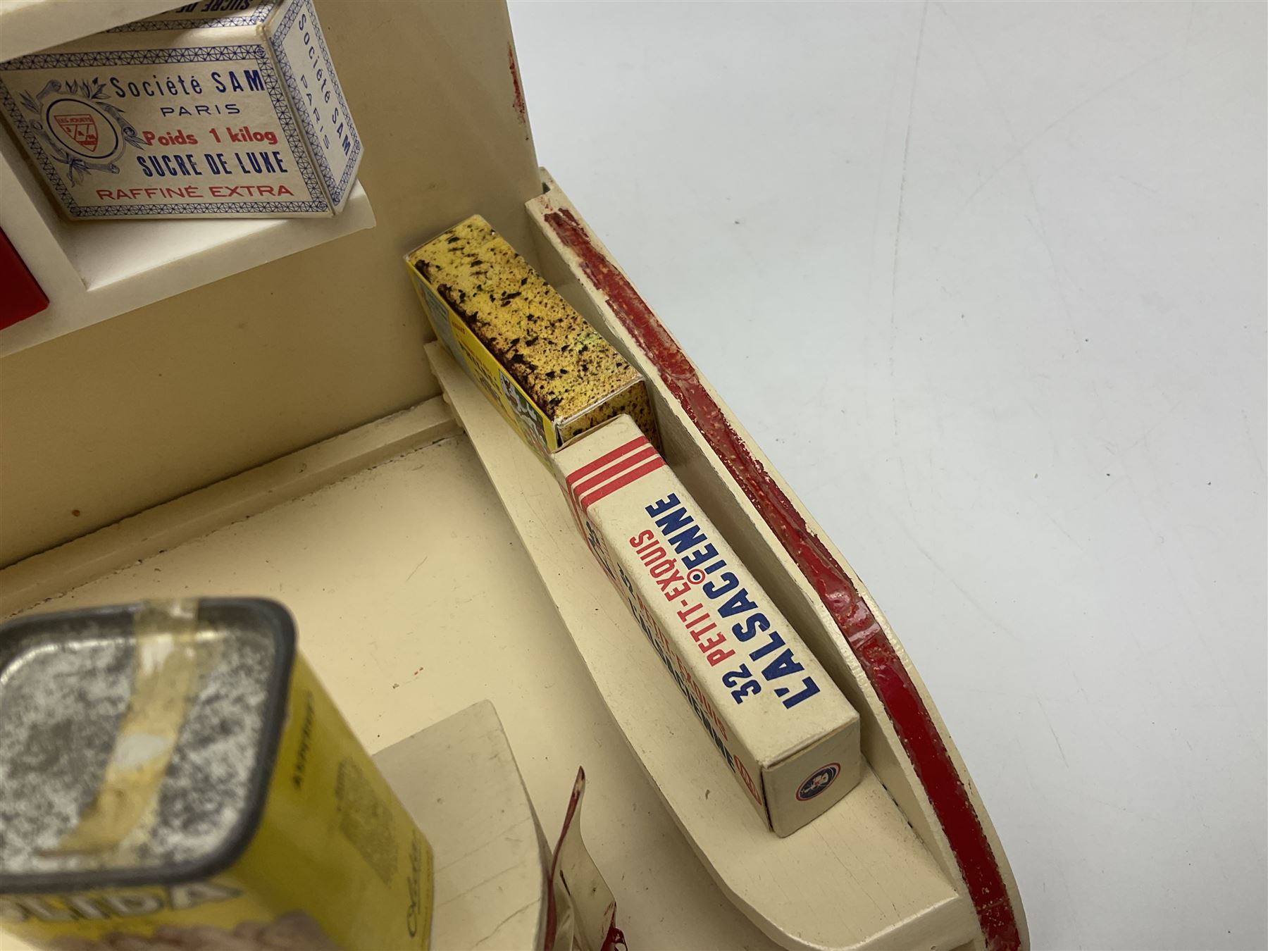 Late 1950s continental red and white painted wooden diorama of a grocery shop interior with fitted shelves and drawers and freestanding 'glazed' counter, fully stocked with miniature tin cans and packets of food L42cm H23cm D22cm