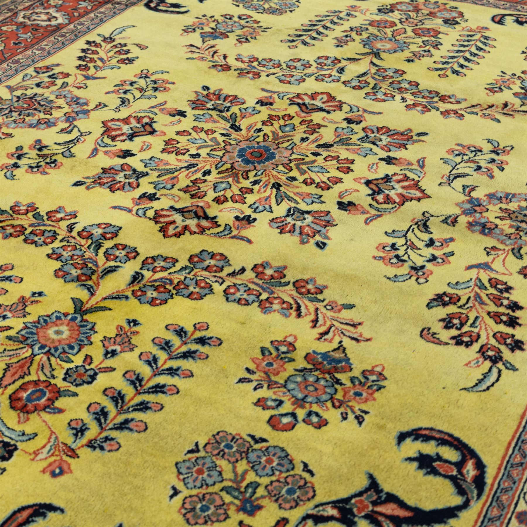 Persian Sarough hand-knotted carpet, golden yellow ground, with an all-over floral design centred by a small floral motif, the field decorated with mirrored flowering sprays, scrolling vines and dark navy foliate corner motifs, enclosed by a terracotta border with repeating flowerheads and palmettes, flanked by narrow guard stripes, with cotton fringes