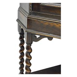 Early 20th century oak corner display cabinet, the moulded canted cornice over a single glazed door with geometric astragal bars, shelved interior, the lower tier forming a triangular platform, raised on four barley-twist supports united by shaped brackets