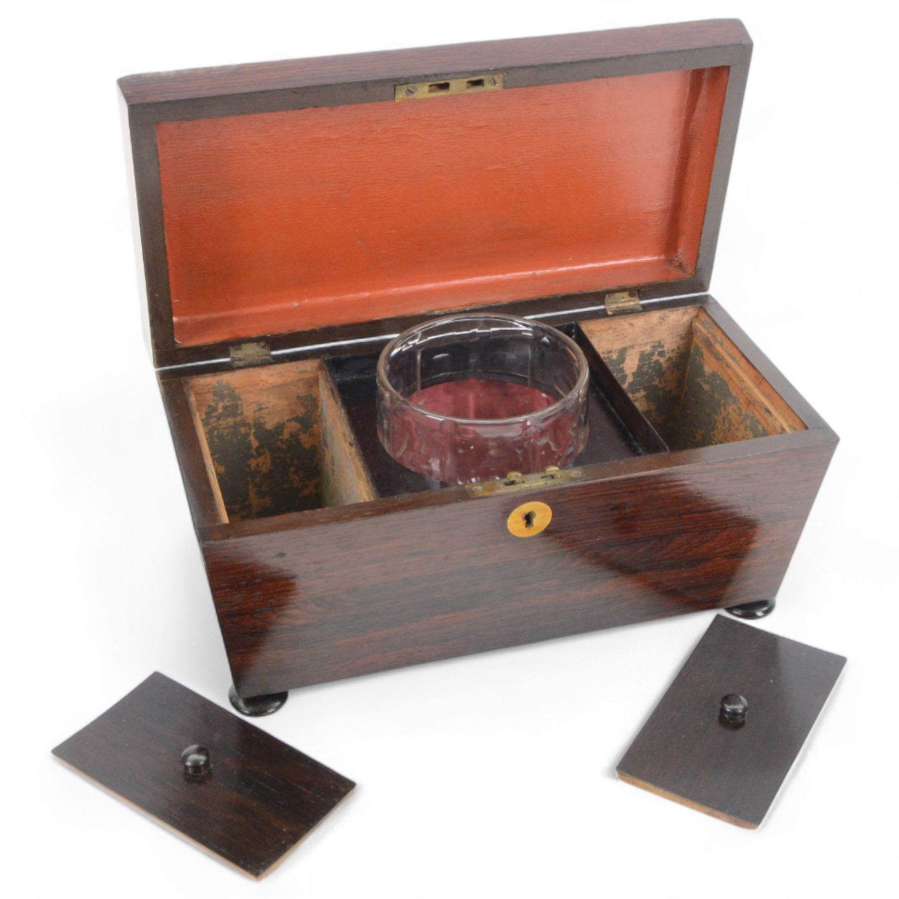 19th century rosewood sarcophagus shaped tea caddy, the hinged lid with brass cartouche to the centre, opening to reveal a fitted interior with central glass bowl flanked and lidded compartments to either side, upon squat bun feet, H17cm