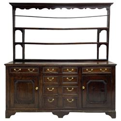 George III oak dresser, the plate rack with shaped frieze over three tiers, the base fitted with four central graduating drawers, the heavily moulded edges designed to appear as eight short drawers, flanked by single drawer over panelled cupboard, on bracket feet