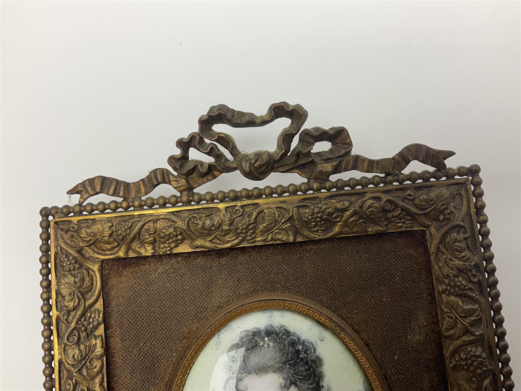 19th century portrait miniature on enamel, depicting a Georgian lady in period dress, hand painted with gilt detailing, in gilt frame with fruiting vine details, overall H13.7cm