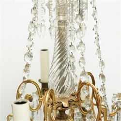Late Victorian gilt bronze mounted crystal chandelier, ceiling rose above shaped top of trailing swags, glass crystal droplets, beneath rising curled branches and glass beads tapering down to five candle sconces, inside circular bezel fitted with drops and glass twist fluted stem, supported with an internal metal shaft above a rococo style stem holding double branches, and similar styled branches, with twelve branches fitted with candle holders and drip trays with crystal drops and cut crystal spears, the underside festooned with crystal glass swags and a bulbous fluted glass terminal and shaped finial with crystal glass swags attached to the branches, the base with pear shaped droplet graduating to the centre, wired for electricity 