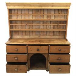 Early 19th century waxed pine farmhouse dresser and rack, the rack featuring two plate shelves and bars above seven drawer base with centre 'dog kennel' recess, raised on turned feet