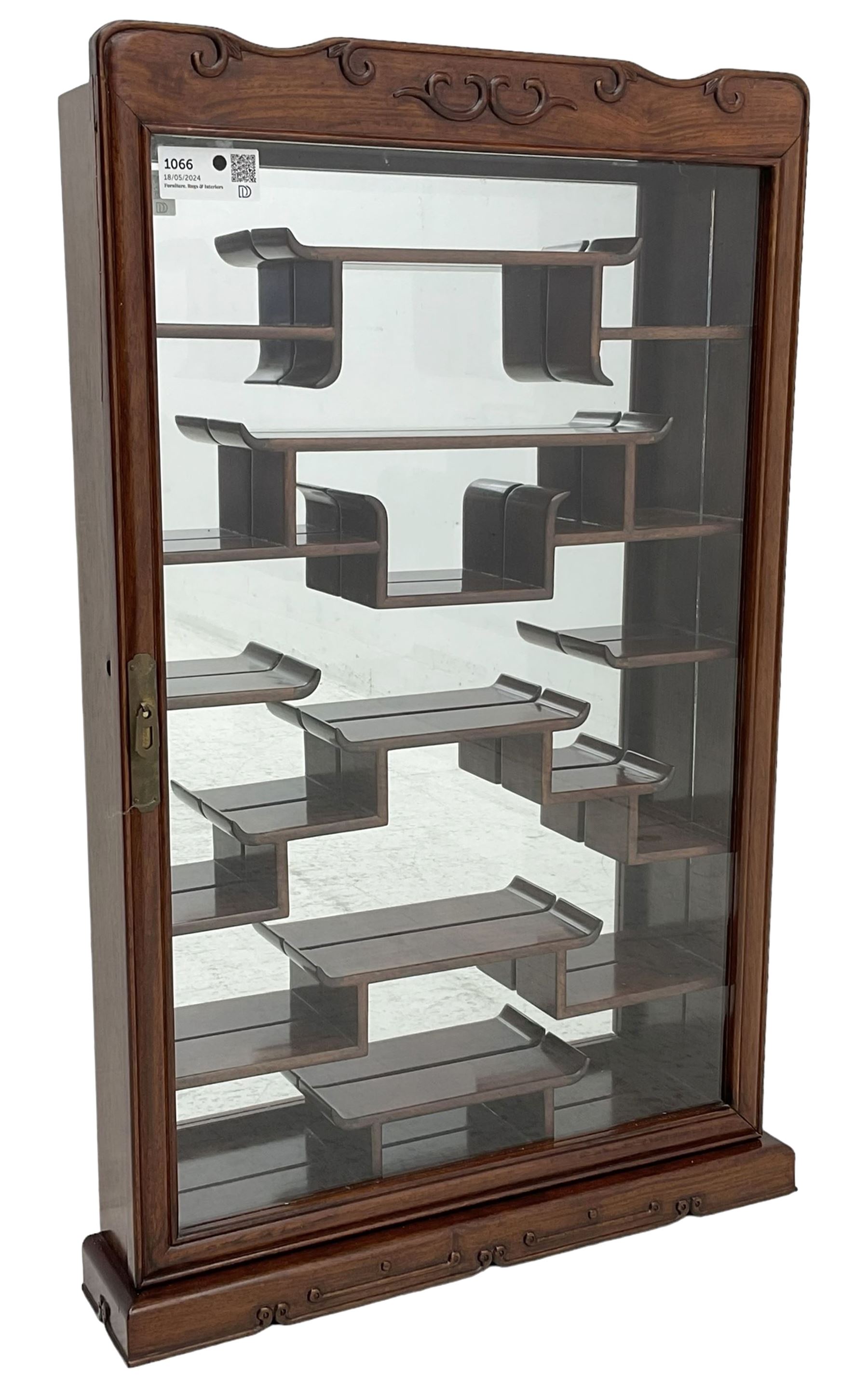 Chinese hardwood wall hanging curio cabinet, the mirror interior fitted with stepped shelves, enclosed by single glazed doors, decorated with carved scrolling foliage 