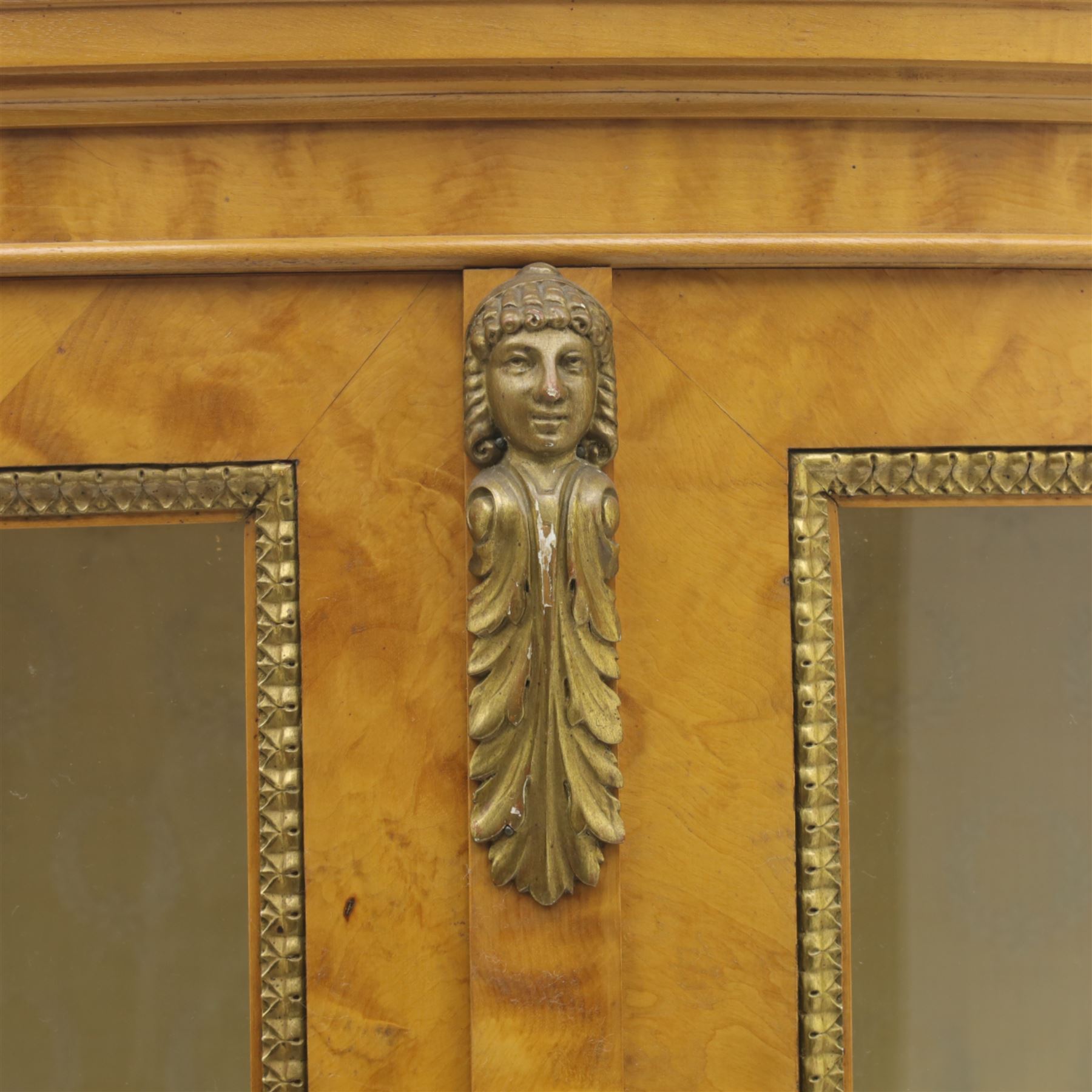 Edwardian satin walnut display cabinet, bowed oval form with moulded and dentil cornice over glazed panels, enclosing a laurel wreath damask interior with adjustable glass shelves, the frame applied with gilt metal bead mouldings and mask mounts, enclosing a shelved interior, raised on cabriole supports with moulded feet