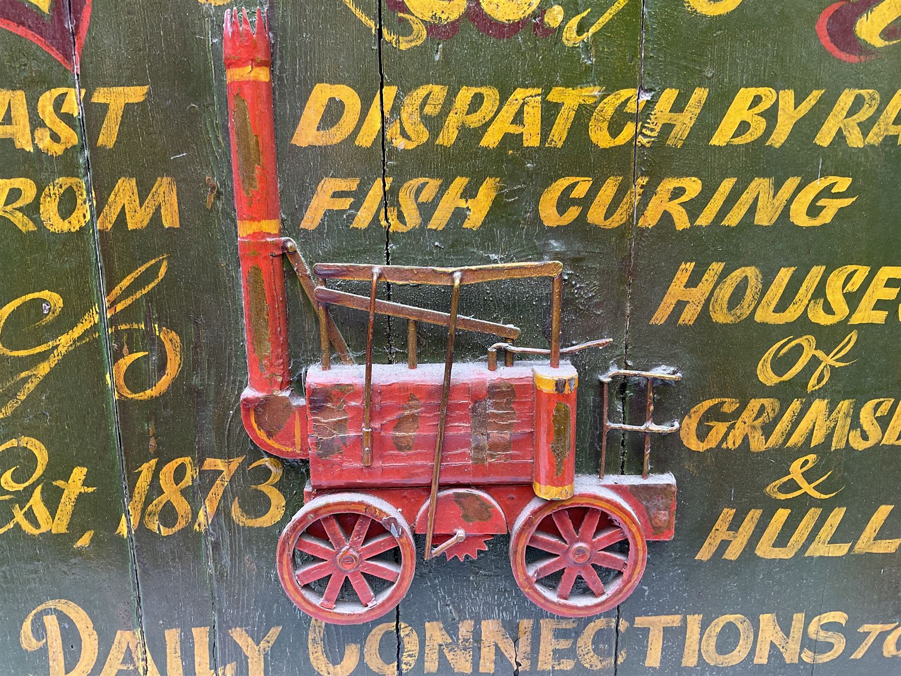 `The Grimsby-York Railroad Co.` painted wooden railway advertising sign 20th century, of planked construction with arched top and moulded border, decorated with an applied wood and metal image of an early steam locomotive in relief, the surrounding wording reading `The Grimsby-York Railroad Co., Fast Dispatch by Rail from Fish Curing Houses of Grimsby & Hull, Est. 1873, Daily Connections to Billingsgate`, 89 x 71cm
