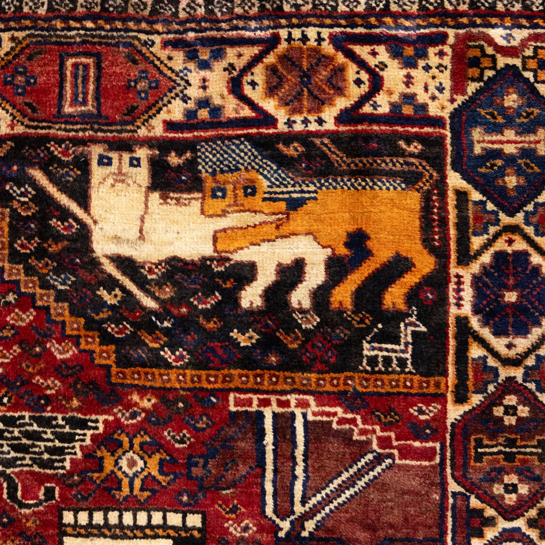 South West Persian Qahqai pictorial hand-knotted rug, madder red field with an all-over pattern of repeating rosettes enclosed with angular leaves and corners with stylized animals figures, central stylized lion in rearing stance and raised forelegs and a human figure shown in profile within a principal border of alternating octagonal and diamond medallions, each enclosing stylized rosettes, flanked by guard stripes incorporating latch hook motifs, with cotton fringe ends  