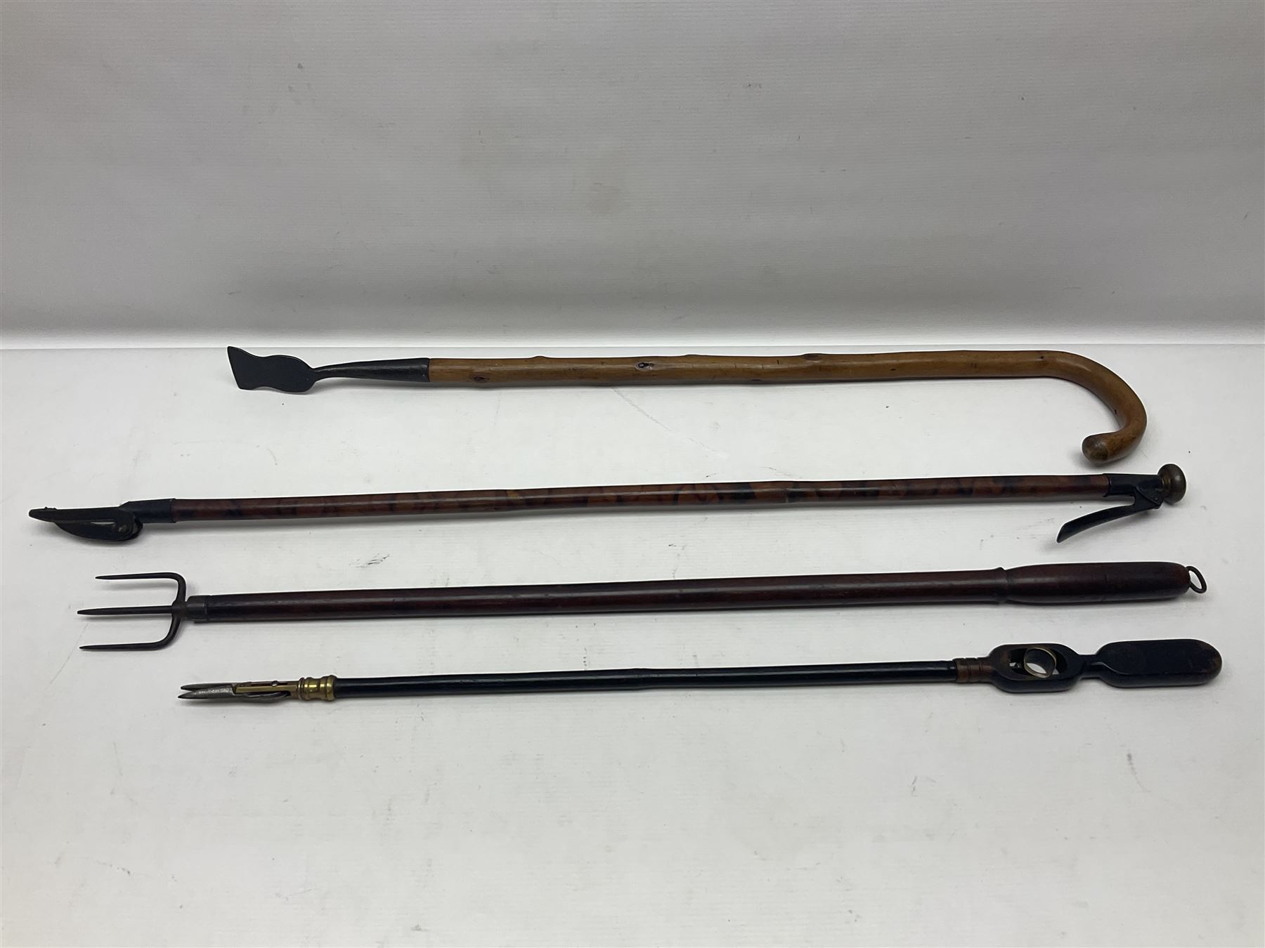 Two late 19th century fruit picker canes, the first example a French ebonised bamboo cane, with pair of fruit scissors to base, the handle stamped Cueille Fruit, the second example with grabbing action, the cap stamped A C Harris, Leicester, together with two other 19th century canes, one with fork and the other with hoe