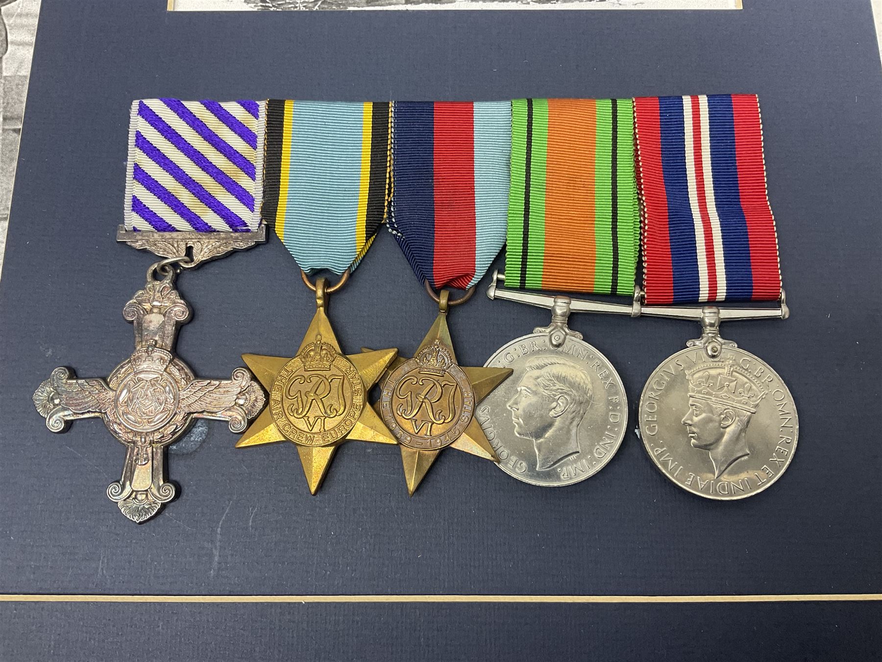 Warrant Officer Gordon Pearce D.F.C. R.A.F.V.R. - display of five medals comprising copy Distinguished Flying Cross, copy Air Crew Europe Star, 1939-45 Star, 1939-45 War Medal and Defence Medal; framed with RAF cap badge, two copy photographs in uniform and copy of investiture letter; mounted and glazed in pine frame 34 x 66cm