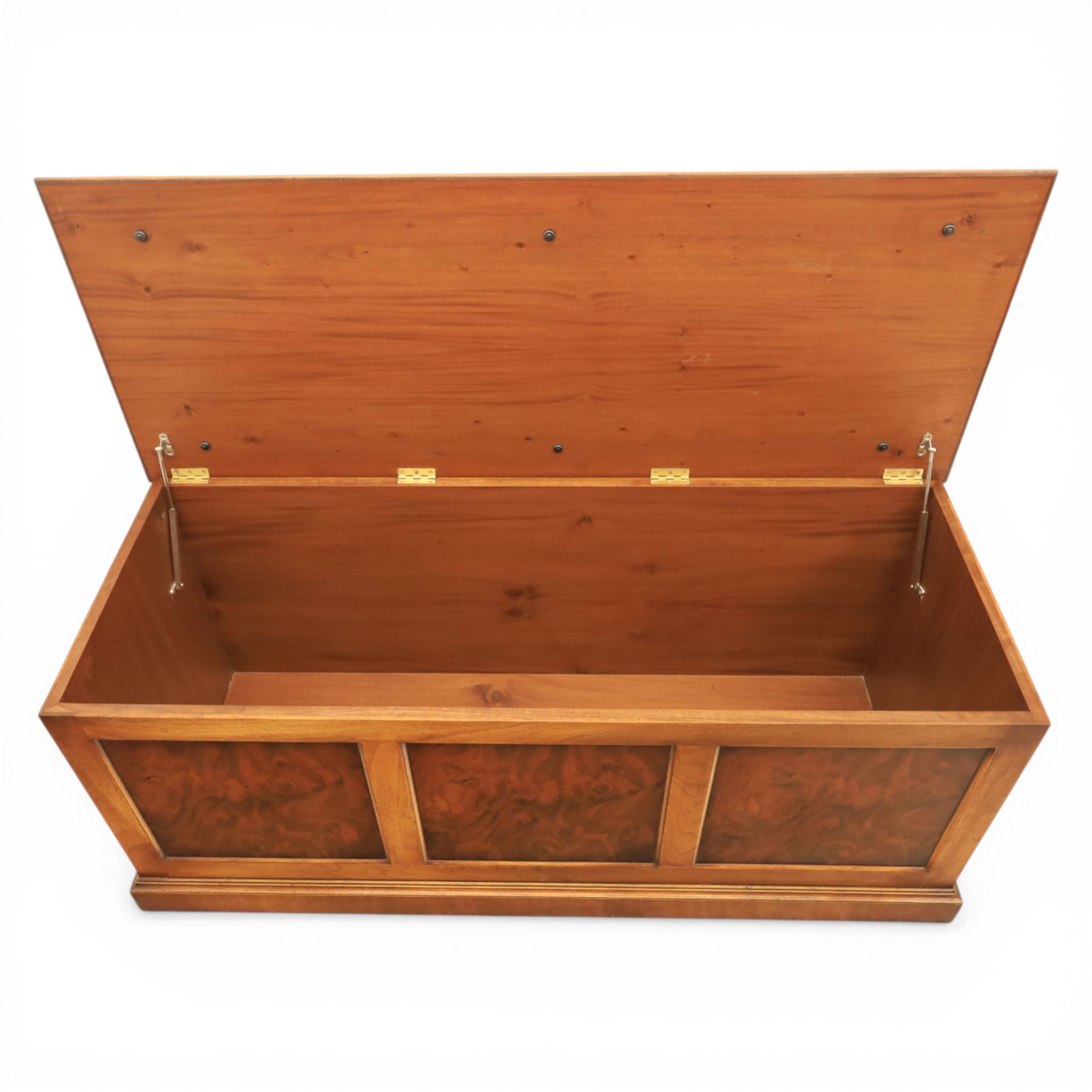 Traditional design figured elm blanket chest, with padded striped upholstered seat, over a hinged top with panelled sections below raised on a plinth base