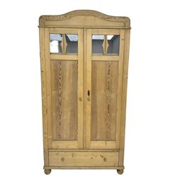 Early 20th century pine double wardrobe, enclosed by panelled and glazed doors, single drawer to base, on turned bun feet