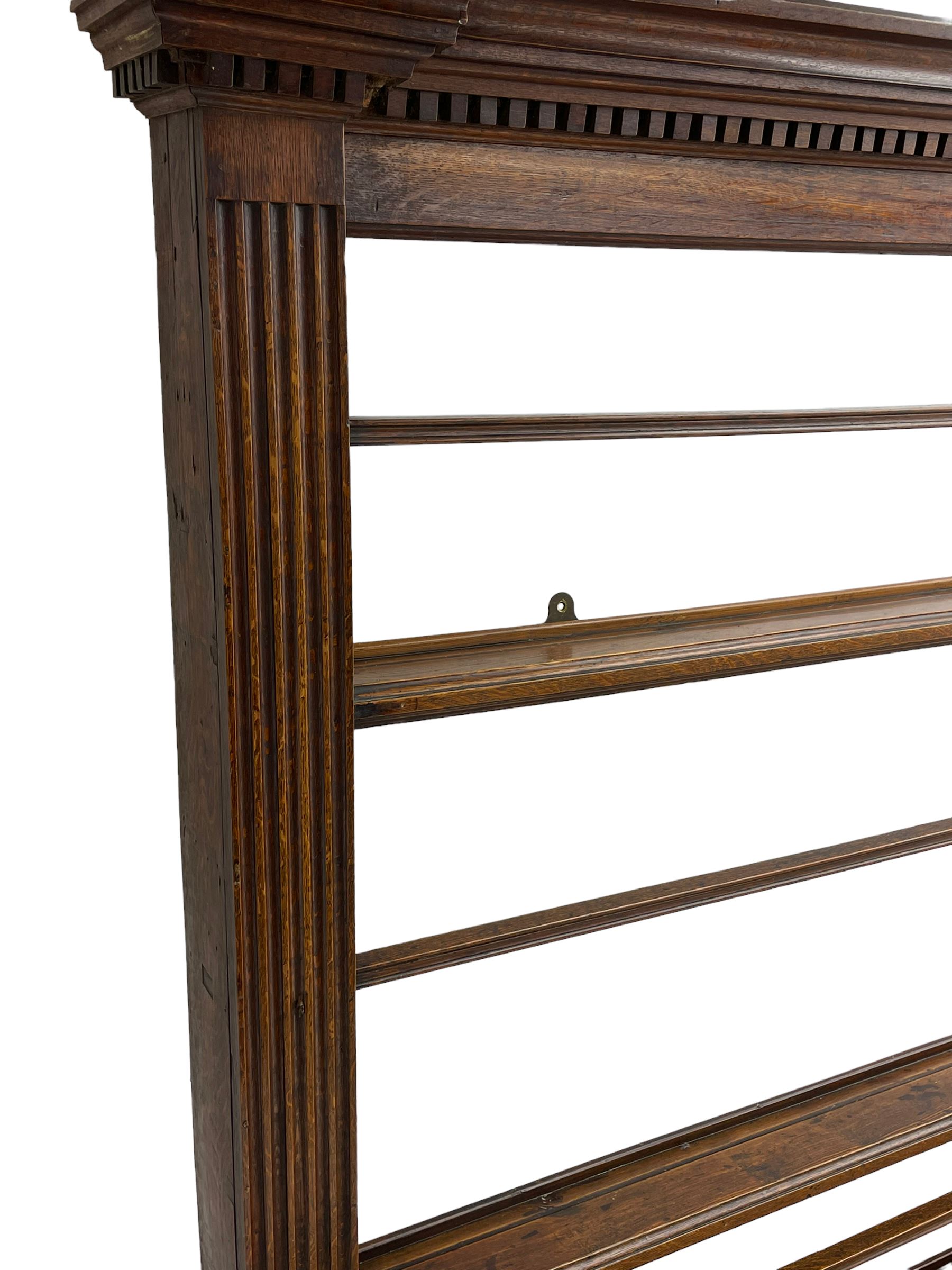 George III oak dresser, projecting dentil cornice over three heights plate rack enclosed by fluted uprights, the dresser fitted with five drawers and two panelled cupboards, canted corners with fluted quarter columns, on bracket feet